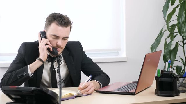 Young guy in a suit speaks on the phone and writes in a notebook 60 fps