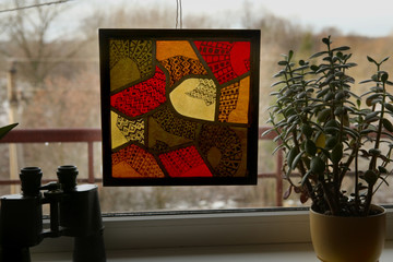 Stained glass with colorful drawing on windowsill. Handmade stained glass graphic picture.