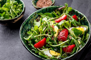 Green leaves and srawberry salad with linen seeds in green bowl, gray background