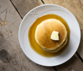Homemade pancakes with maple syrup on the white plate on the wooden table