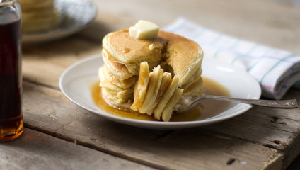 homemade pancakes with maple syrup and butter on the white plate eaten with fork 