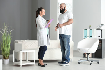 Fototapeta premium Young female doctor measuring weight of overweight man in clinic