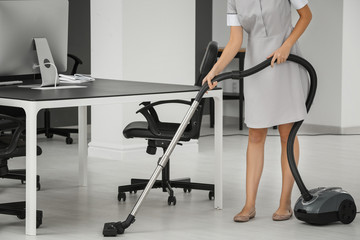 Young woman hoovering floor in office using vacuum cleaner