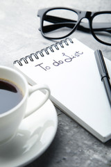 To do list in notepad with cup of coffee and glasses on grey wooden table