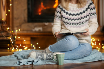 Young woman relaxing while reading book in living room decorated for winter holidays