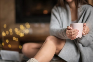Young woman relaxing while drinking tea in living room decorated for winter holidays