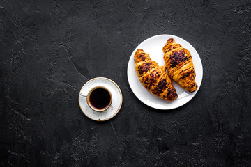 Light breakfast. Small cup of black coffee and croissant on black background top view copyspace