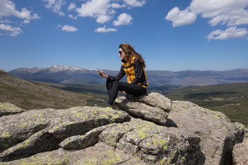 sport hiking or trekking woman with yellow and black clothes, sitting on rock peak, typing mobile...