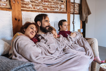 Happy family at home watching movies in the couch and eating popcorn .