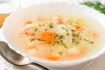 Chicken soup with stelline pasta and carrot on white wooden table.