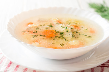 Chicken soup with stelline pasta and carrot on white wooden table.