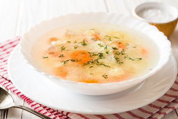 Chicken soup with stelline pasta and carrot on white wooden table.