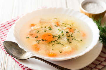 Chicken soup with stelline pasta and carrot on white wooden table.