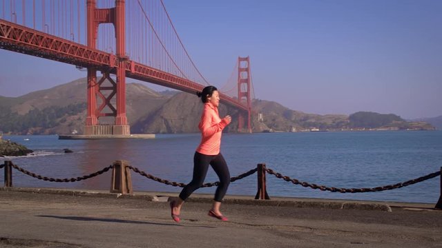 Asian woman jogs in San Francisco. The Golden Gate Bridge can be seen in the background.