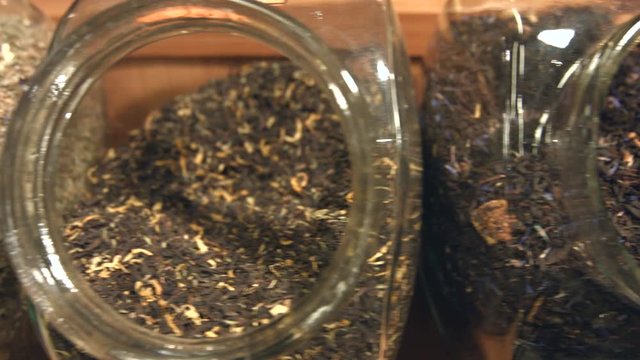 Varied varieties of flavored tea with additives.
Top view. The camera moves ( from left to right ) over the jars in which there are different kinds of tea.