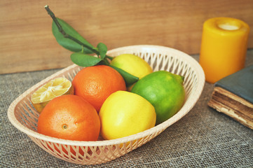 Citrus fruits in basket near candle on wooden background. Oranges, limes and lemons.