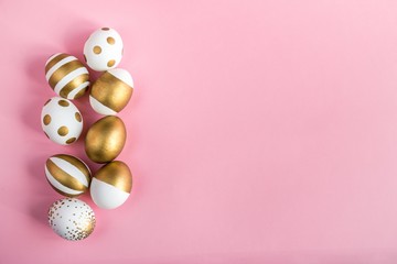 Top view of easter eggs colored with golden paint. Various striped and dotted designs. Pink background.