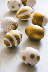 Close up of easter eggs colored with golden paint. Various striped and dotted designs. White wooden background.