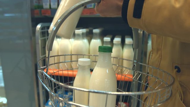 Bottled milk on the shelf in the store.
The man's hand takes a bottle of milk from the shelf and puts it in the basket.