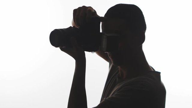 Silhouette of Photographer close-up. Young man takes pictures with DSLR camera isolated on white background
