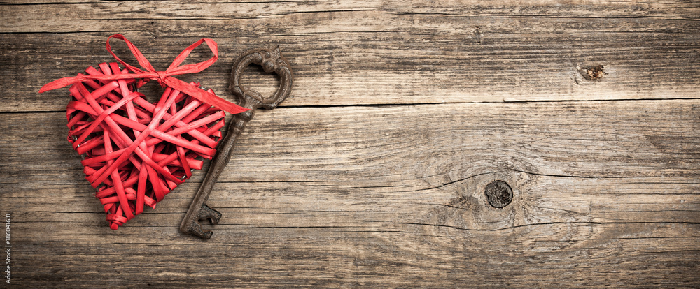 Wall mural red wicker heart and vintage key on wooden background