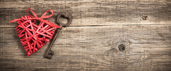 Red wicker heart and vintage key on wooden background