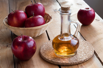 A bottle of apple cider vinegar with red apples on a wooden table