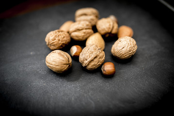 Mixed whole nuts in their shells including walnuts, hazelnuts, almonds and pecans shot on black slate