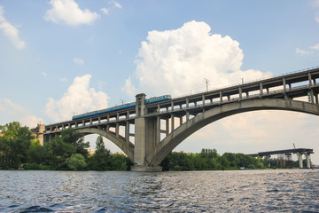 Fototapeta na wymiar A train is riding over a bridge over a river against a blue sky