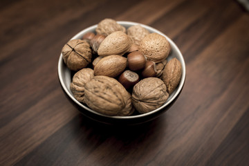 A bowl of mixed whole nuts in their shells including walnuts, hazelnuts, almonds and pecans with a short depth of field