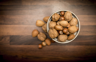 A bowl of healthy mixed whole nuts in their shells including walnuts, hazelnuts, almonds and pecans shot from above