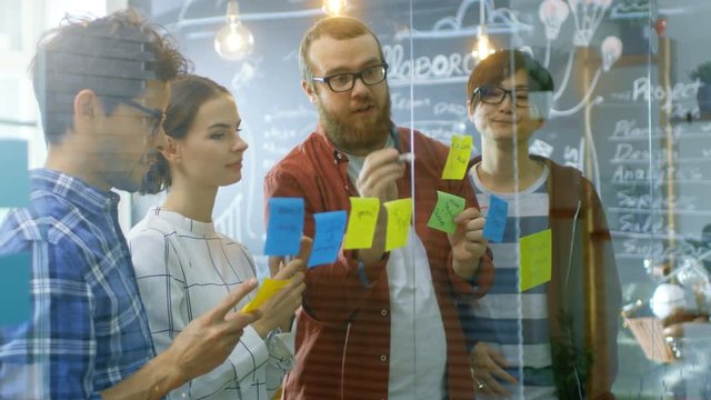 Diverse Team of Young Developers Brainstorming, They Have Discussion and Use Glass Board and Sticky Papers to Conceptualize Their New Plan. Shot on RED EPIC-W 8K Helium Cinema Camera.