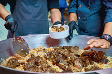 Two cooks in uniform prepare Uzbek pilaf from lamb. Plav is an excellent dish and cooked on the grill in the open air.