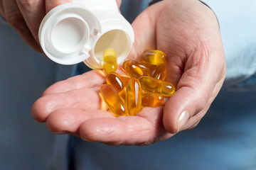 Woman hand holds yellow medication capsules of omega 3, pours from a white bottle into palm the fish oil, healthy supplement pills