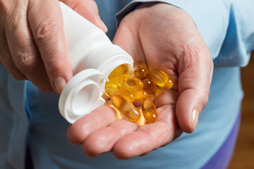 Woman hand holds yellow medication capsules of omega 3, pours from a white bottle into palm the...