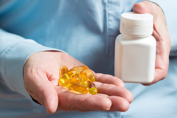 Yellow medication capsules of omega 3, fish oil, healthy supplement pills in the woman palm hand...