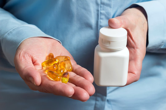 Yellow medication capsules of omega 3, fish oil, healthy supplement pills in the woman palm hand and white plastic bottle in the other hand