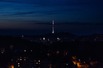 a bright tall tower on the background of a city that falls asleep under the influence of the onset of the night
