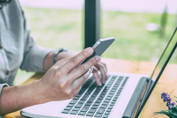 Close Up of woman hands using mobile phone and laptop computer with blank copy space screen for your advertising text message or content business at a coffee shop with a document.