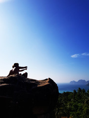 Silhouette couple sitting on the top of mountain over blue sea and sky background