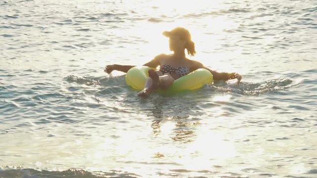 A happy girl is swimming at dawn. A girl in an inflatable circle and the sea on a sunny path.