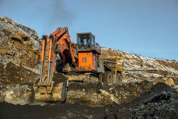 Obraz premium Big yellow dump truck and excavator in coal mine at sunrise 