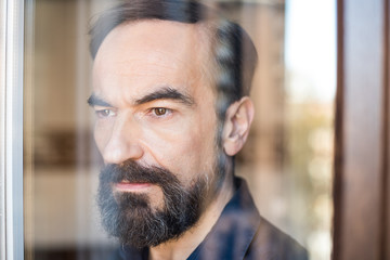 Portrait of a mature man posing thoughtful throughout the window    .