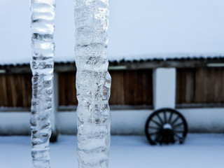 Large ice icicles on a cornice with decorative wagon wheel base under wooden windows. Series of...