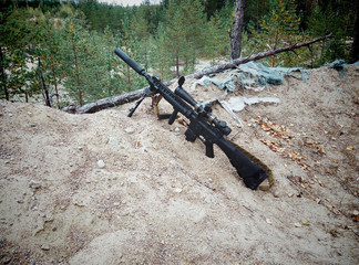 Assault rifle on the background of pine forests and sand