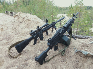 Assault rifle and machine gun on the background of pine forests and sand