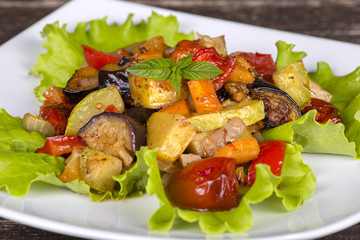 Stewed vegetables in a white bowl on wooden table. Close up