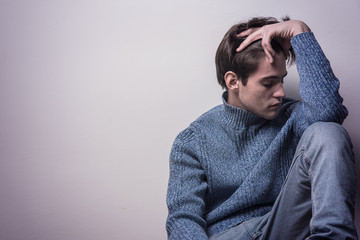 Depressed young man sitting in a corner by himself, feeling sad and lonely