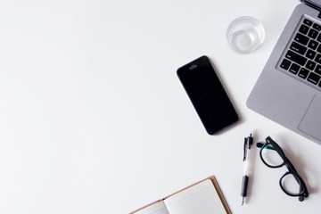 White office desk table with laptop, smartphone, notebook, and glass. Top view with copy space, flat lay.