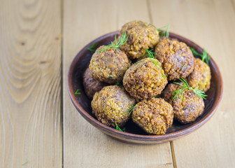 Freshly made falafel in a clay bowl with herbs on a wooden table.